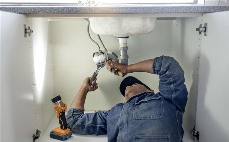 Plumber repairing pipes beneath a bathroom sink in Palm Bay