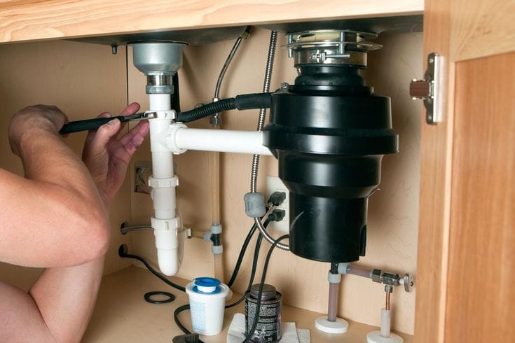Plumber installing a garbage disposal beneath a kitchen sink in Palm Bay