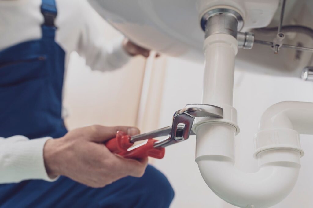Plumber repairing a white drain pipe beneath a sink in Palm Bay